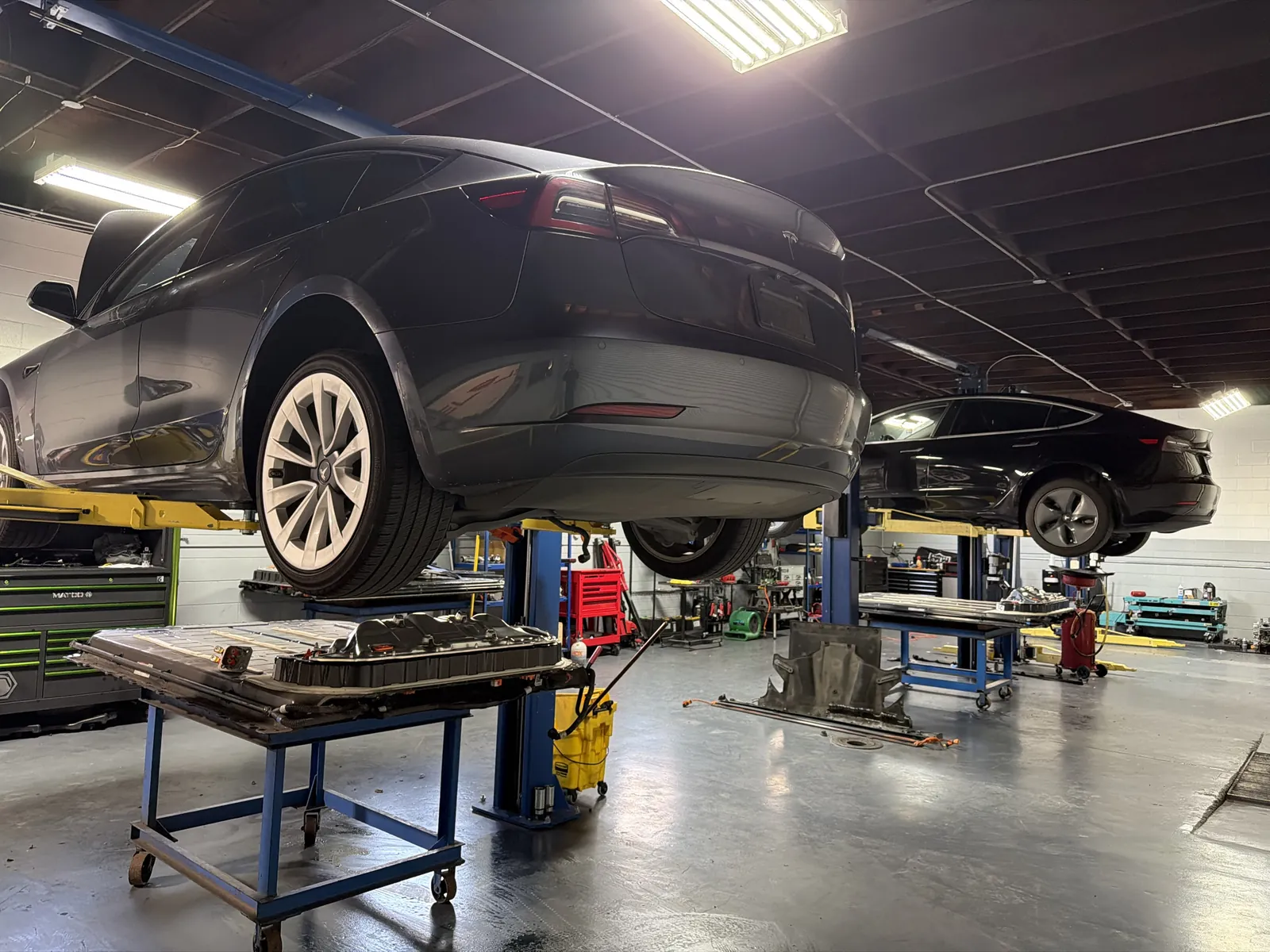 Tesla Model 3 on the lift with its high-voltage battery pack removed for repair